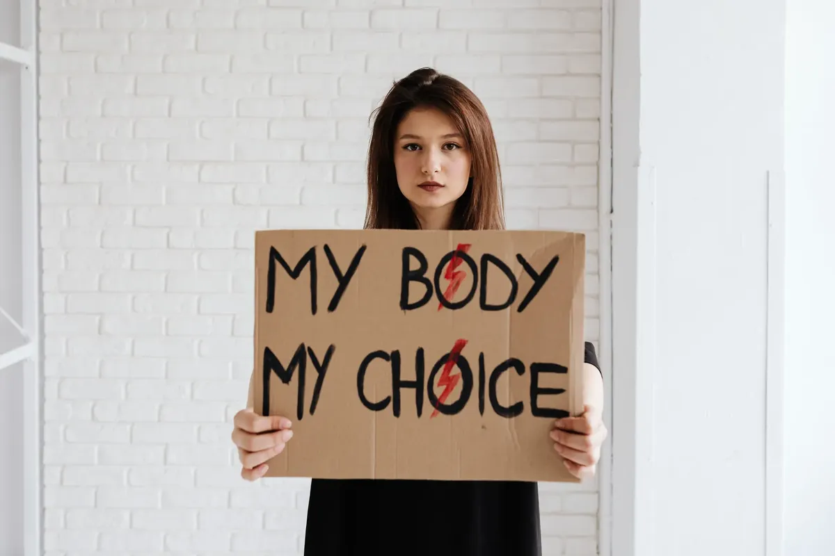 Teenage girl holding 'My Body My Choice' sign advocating women's rights indoors.