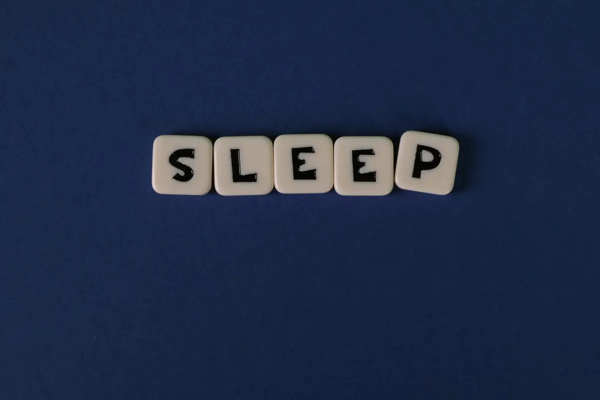 黒いネイビーの背景に白い文字タイルが 'SLEEP' と書かれており、シンプルで休息を促す意図を強調している。