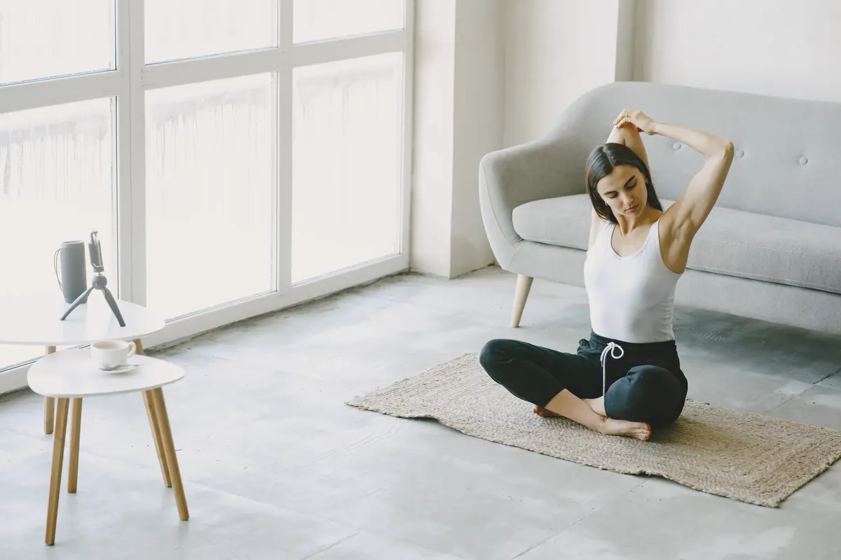 Woman in casual attire stretching during yoga at home in a bright, modern living room.