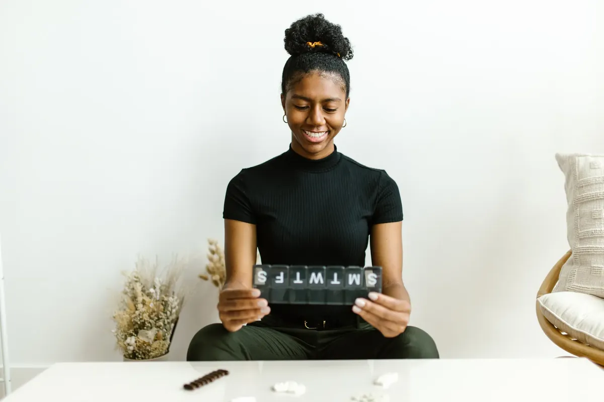 Black woman smiling while holding a weekly pill container, promoting health awareness.