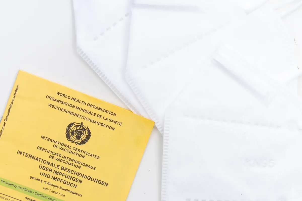 A WHO vaccination card alongside KN95 masks on a white surface, symbolizing health protection and safety.