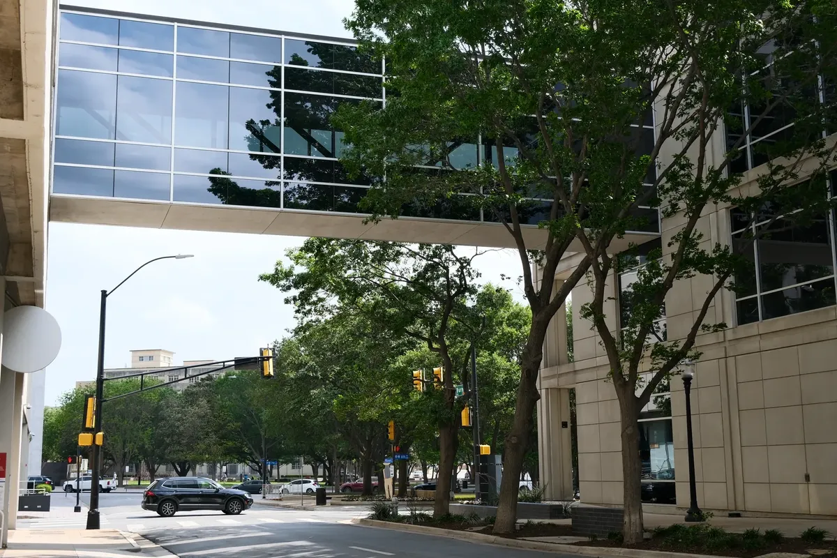 Modern urban scene in Fort Worth, Texas, featuring a glass skybridge and tree-lined street.